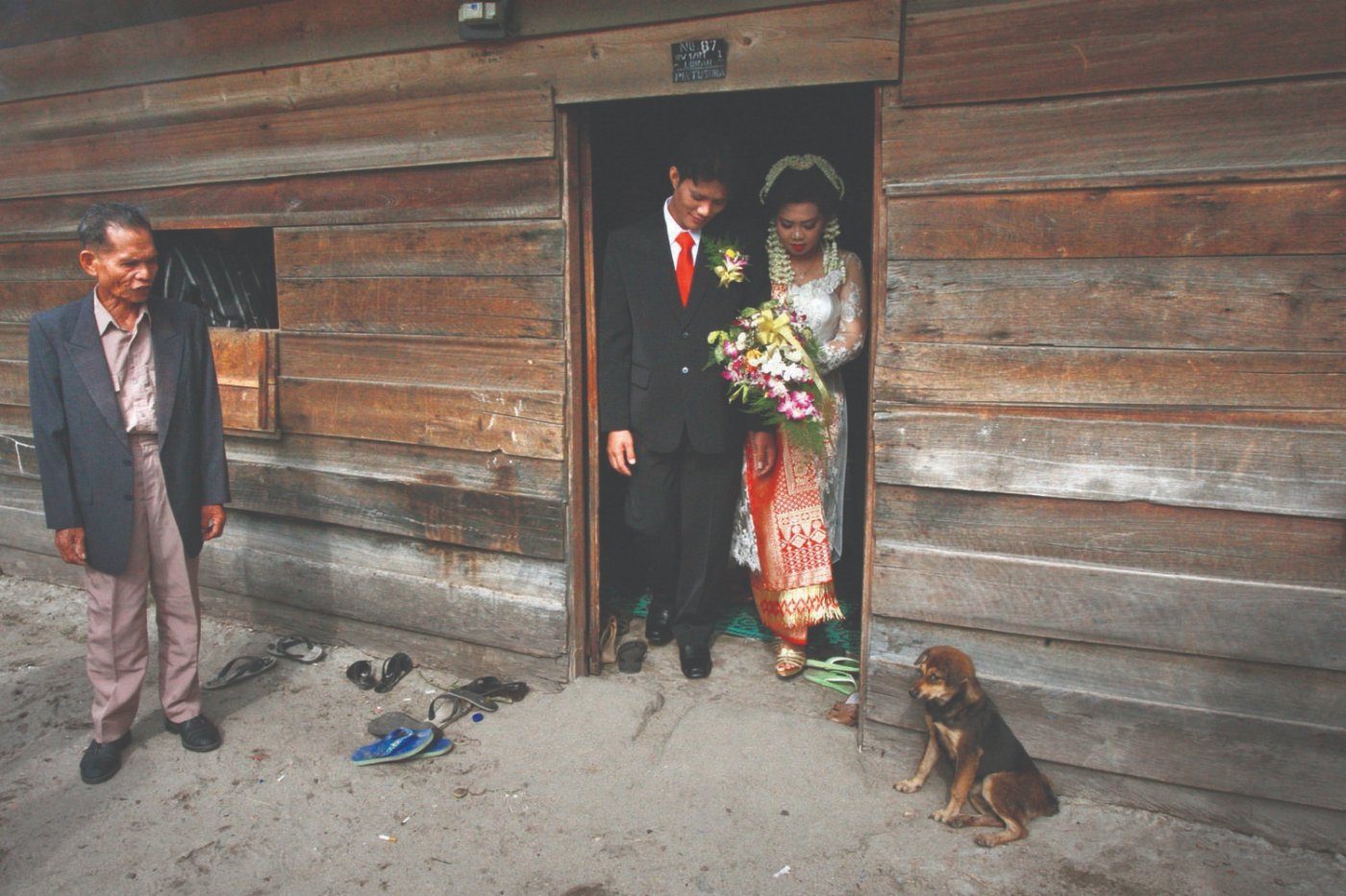 A bride and groom stepping out of a wooden house on their wedding day, Pangururan