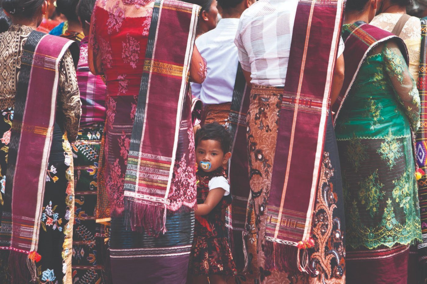 A child among rows of adults in ulos shawls at the Sipahalima ceremony, Laguboti