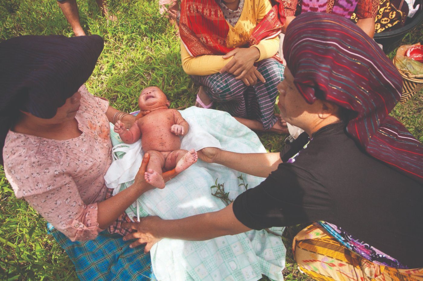 Two women in Karo headdress holding a newborn at the Sirembah Ku Lau ritual, Tanah Karo