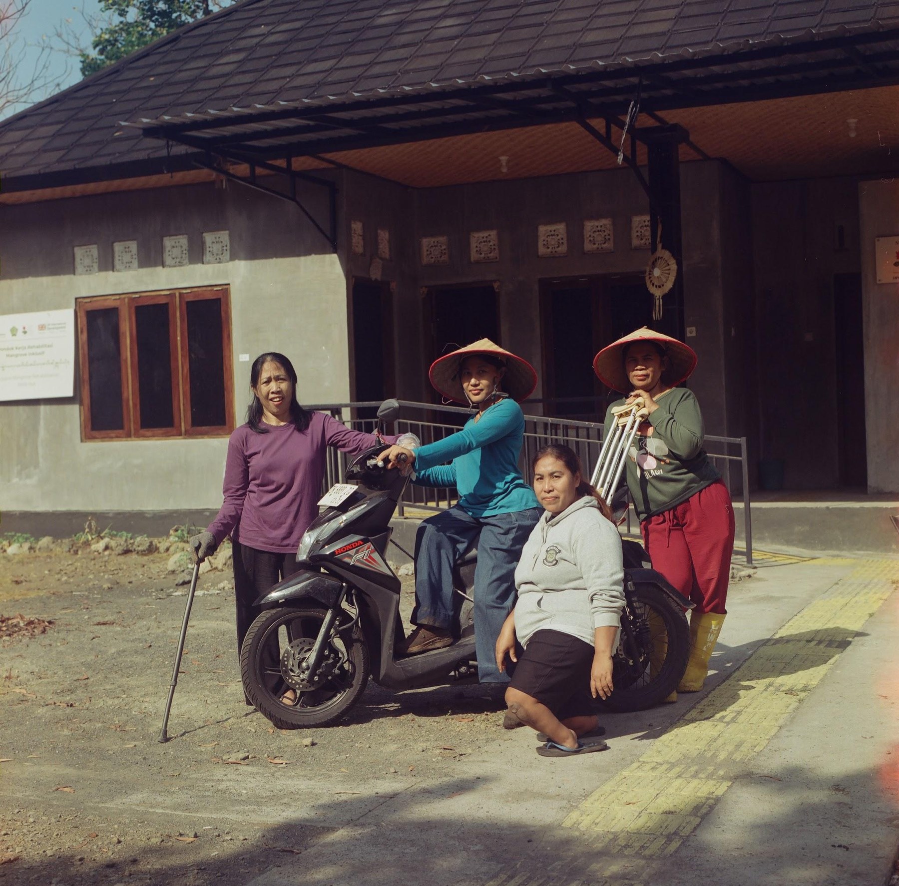 Four women of HWDI Jembrana with a motorbike in front of their multipurpose hut