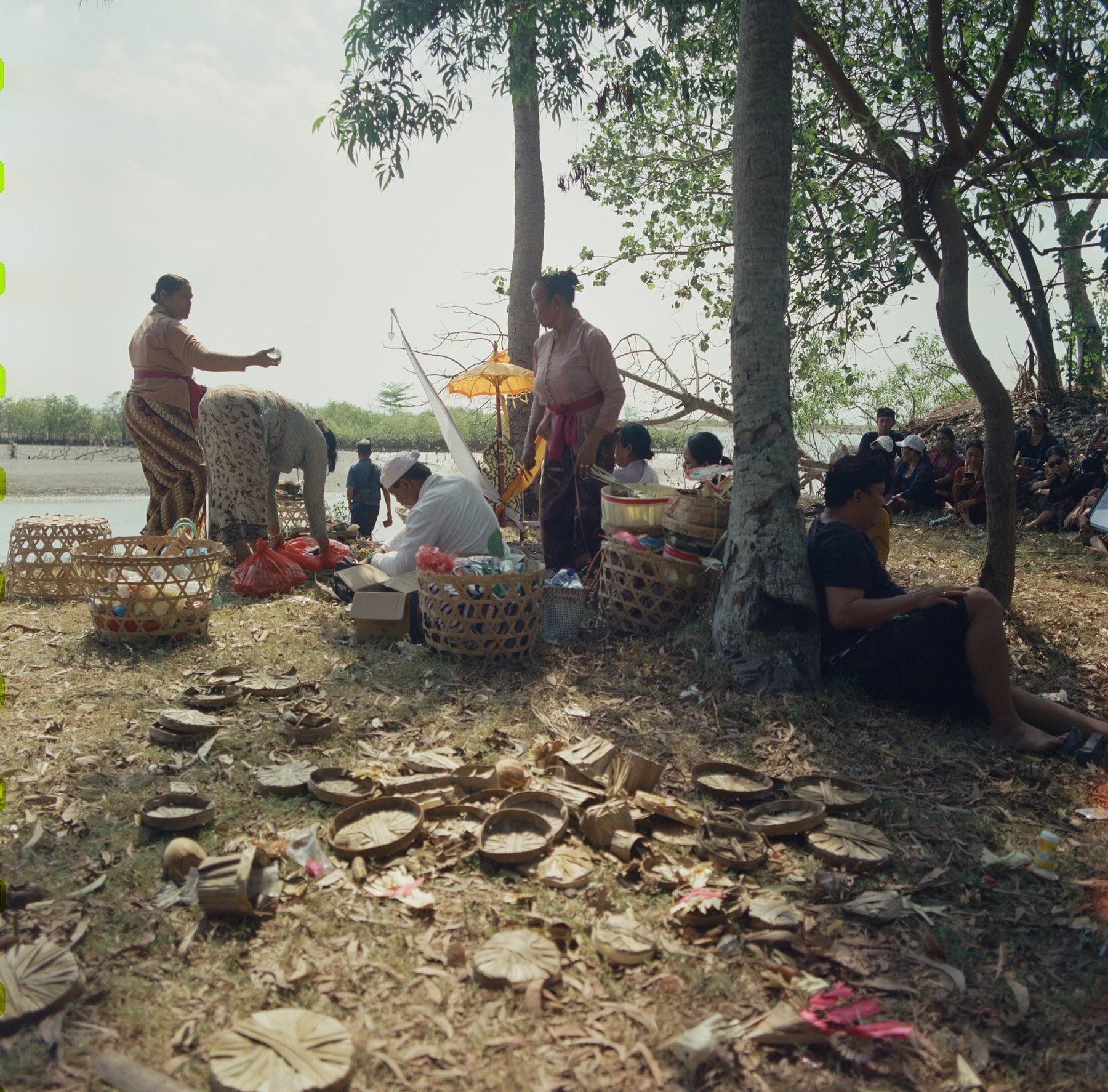 Families and priests with offering baskets under the trees on the mangrove shore