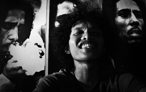 A young man laughing between two posters of Bob Marley