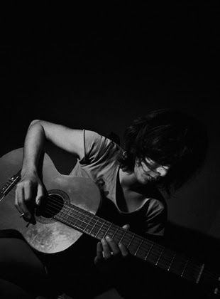 A young man playing an acoustic guitar in the dark
