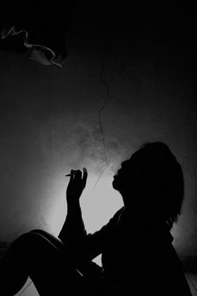 Silhouette of a seated figure holding a cigarette against a pale wall