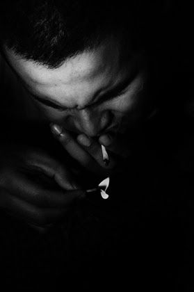 A man lighting a cigarette with a match, his face lit from above
