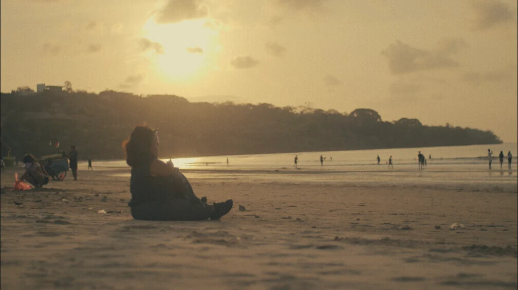 A figure sitting on the sand watching the sunset over the sea, from Terpejam untuk Melihat